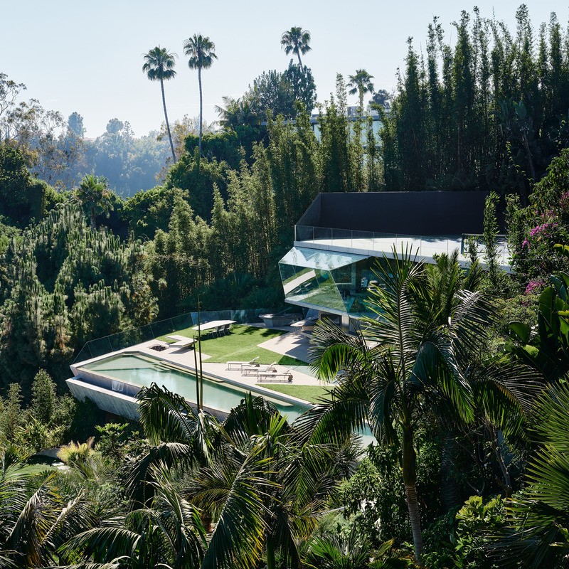 Le Club James, complexe accessoire récemment achevé, émerge du paysage luxuriant de la jungle, ses géométries cristallines jouant avec la flore sauvage environnante et le ciel bleu vif de la Californie du Sud. Le toit du court de tennis à débordement se t