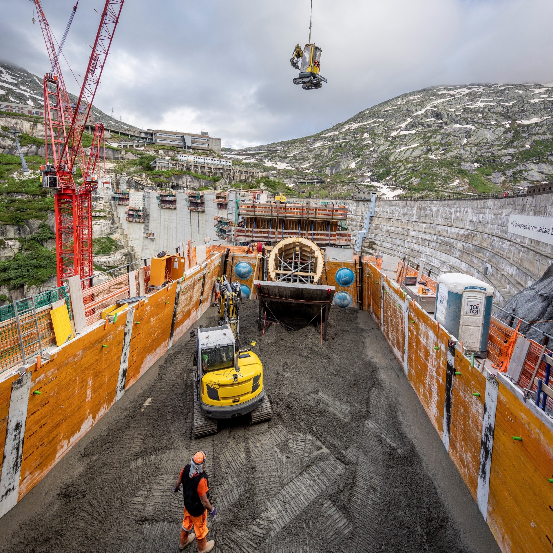 Chaque couche de béton mesure 3 m de hauteur. Le béton est réparti à l'aide d'une petite pelleteuse et compacté par une seconde pelleteuse équipée de vibropointes.