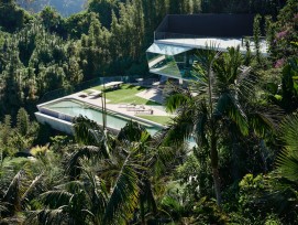 Le Club James, complexe accessoire récemment achevé, émerge du paysage luxuriant de la jungle, ses géométries cristallines jouant avec la flore sauvage environnante et le ciel bleu vif de la Californie du Sud. Le toit du court de tennis à débordement se t